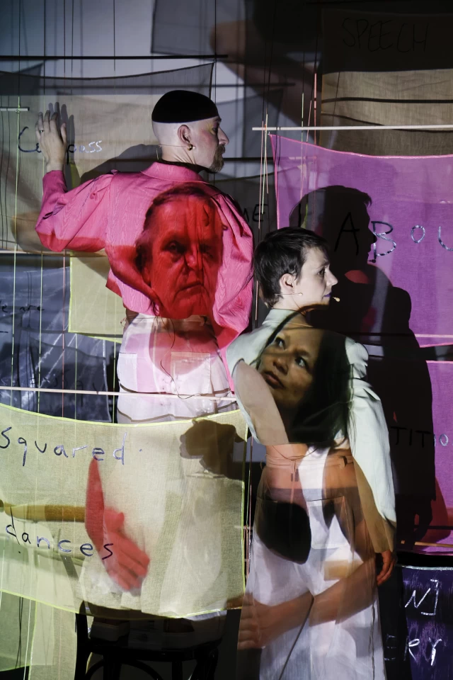 Britta and William moving banners with Margaret and Justine in video projection performing the Colin and Margaret pose from a photograph, Tanzfabrik Berlin, June 2021 – photo by Anja Weber