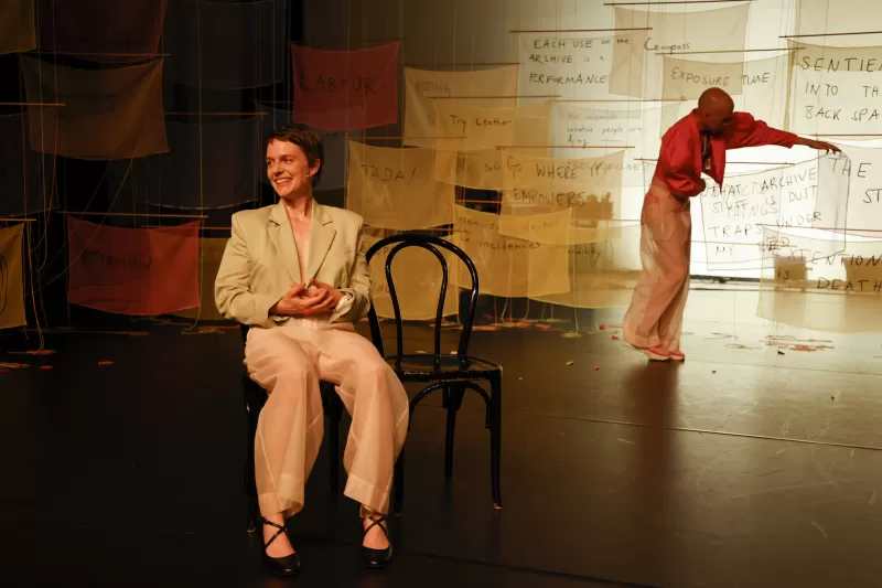 Britta explaining the recipe card "That Archive Stuff Is Dust Traps Under My Bed" with William holding the corresponding banner, Tanzfabrik Berlin, June 2021 – photo by Anja Weber