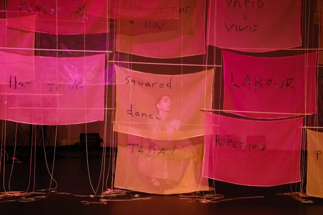 Britta squatting behind banners, Tanzfabrik Berlin, June 2021 – photo by Anja Weber